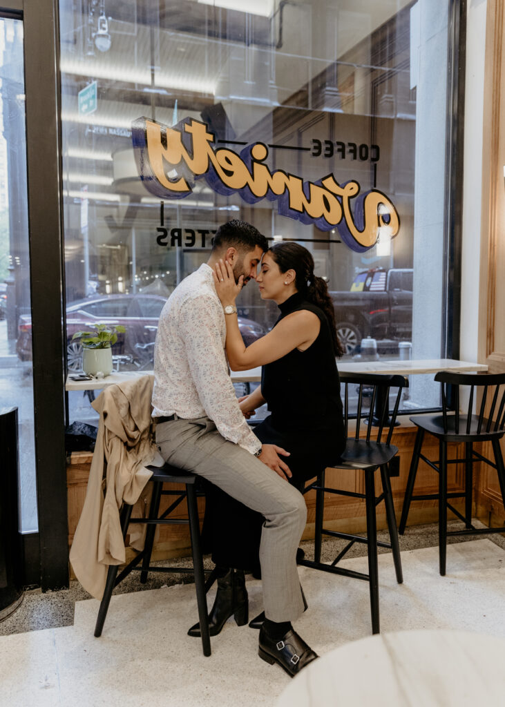 Romantic and playful couple sitting in a coffee shop for their engagement photos in NYC